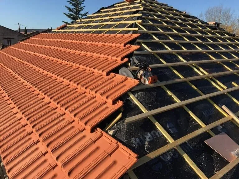 Pose de tuiles neuves sur un liteaunage jaune, chantier de réfection de toiture